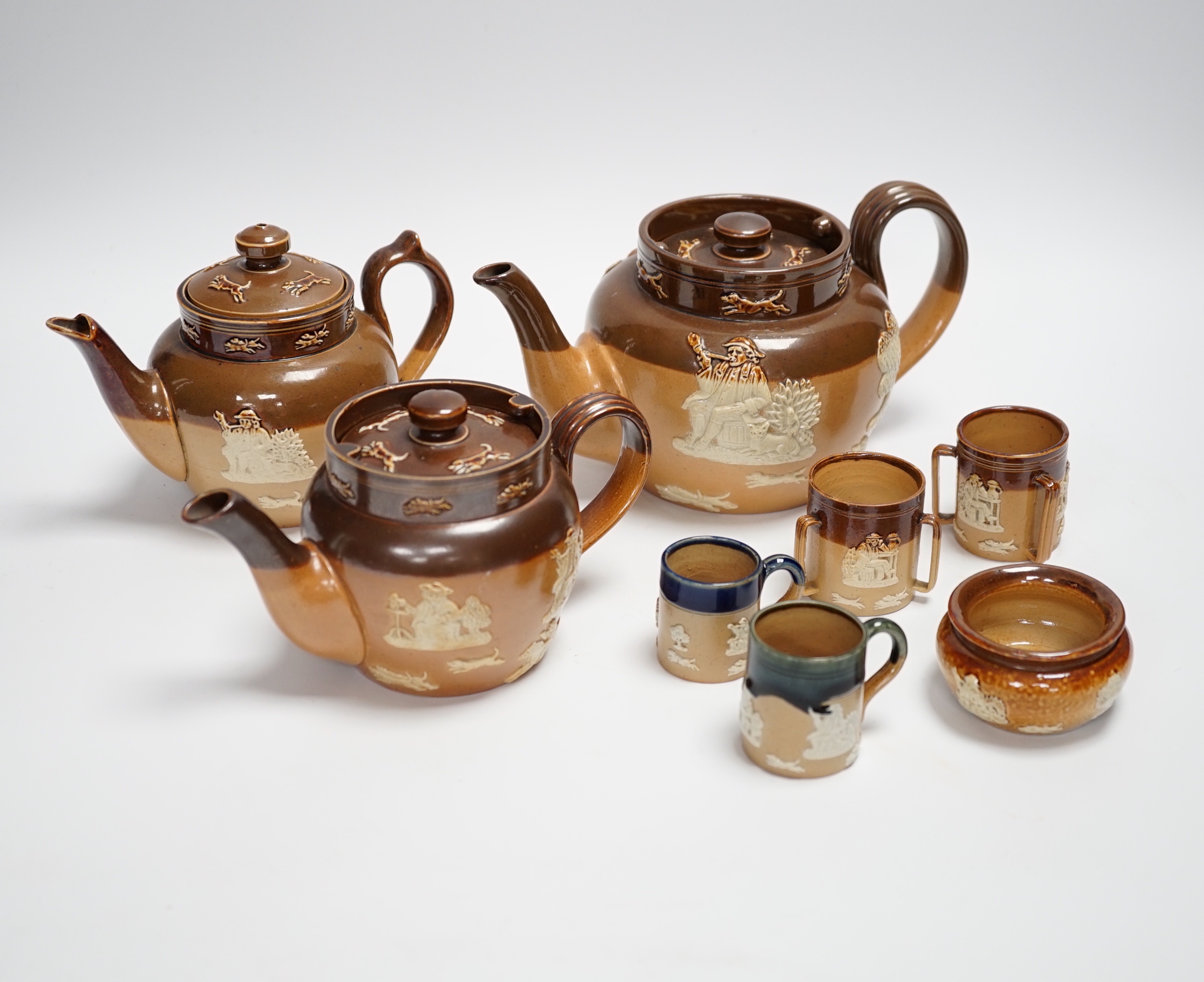 An assortment of Doulton stoneware including teapots, miniature tygs and twin handled pots, some silver mounted, largest 22cm wide